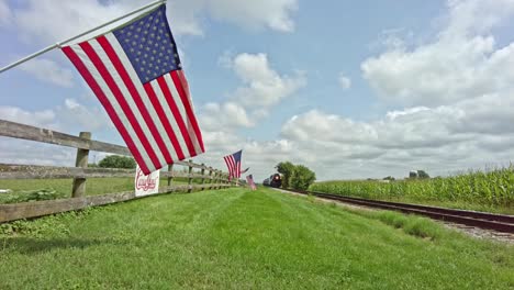 Ein-Niedriger-Engel-Einer-Dampfmaschine-Und-Personenwagen-Nähern-Sich-An-Einem-Schönen-Tag-Mit-Einer-Reihe-Amerikanischer-Flaggen,-Die-Die-Annäherung-Säumen