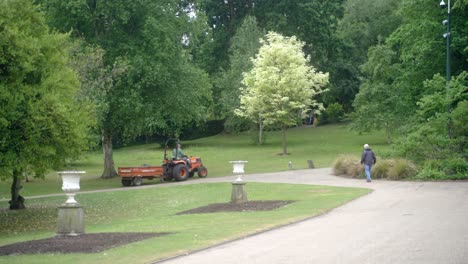 Toma-Panorámica-De-Mano-De-Una-Cortadora-De-Césped-Con-Asiento-Naranja-Con-Remolque-Conduciendo-A-Través-De-Los-Jardines-Botánicos-De-Sheffield,-Inglaterra