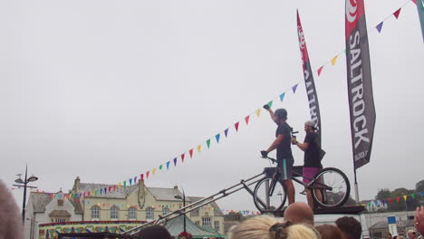 Hombre-Filmando-Ciclista-Experto-Realizando-Acrobacias-En-Una-Bicicleta-Durante-Un-Espectáculo-De-Acrobacias-En-Bicicleta-De-Montaña-En-Truro,-Cornualles,-Inglaterra