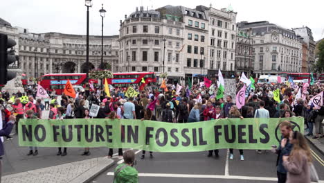 Extinction-Rebellion-Klimawandel-Demonstranten-Halten-Ein-Grünes-Banner-Mit-Der-Aufschrift-„Keine-Zukunft-In-Fossilen-Brennstoffen“,-Während-Hunderte-Sich-Darauf-Vorbereiten,-Am-Ersten-Tag-Der-Proteste-Mit-Fahnen-Und-Plakaten-Zu-Marschieren