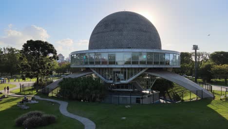 Establecimiento-De-Una-Panorámica-Aérea-De-Bajo-Nivel-Alrededor-De-Un-Edificio-En-Forma-De-Ovni,-Planetario-Galileo-Galilei-A-La-Luz-Del-Día-Brillante-Con-Rayos-De-Sol-Asomados-A-Través-De-La-Estructura,-En-El-Parque-Tres-De-Febrero,-Buenos-Aires