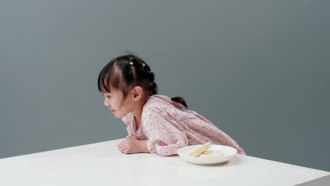 Child-with-dress-hanging-at-white-table-with-dish-with-candy