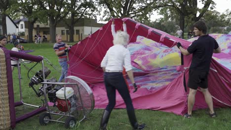 Group-Of-People-Inflating-Hot-Air-Balloon-With-Cold-Air-From-A-Large-Fan-At-The-Park-In-Valmiera,-Latvia