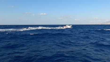 Dinghy-rubber-boat-with-tourist-on-board-navigating-on-sea-water-at-high-speed-leaving-white-wake-trail-seen-from-another-cruising-vessel