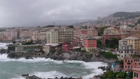 Rough-sea-waves-hitting-rocky-coastline-of-Genoa-city-with-dark-cloudy-sky,-aerial-orbit-view