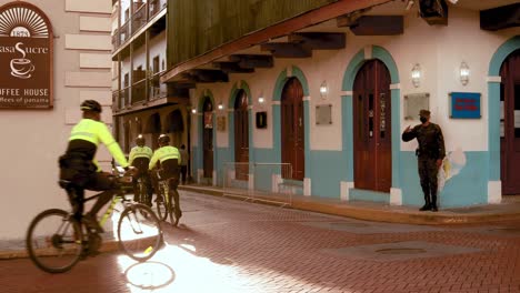 Police-Officers-on-mountain-bikes-riding-through-the-city-streets-of-Casco-Viejo,-saluting-a-fellow-officer-as-they-turn-a-corner-on-their-morning-patrol,-Panama-City