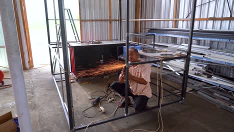 Person-using-angle-grinder-to-clean-metal-frame,-static-view