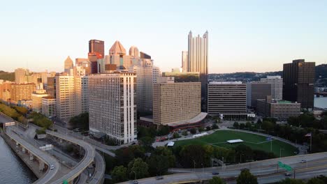 Vista-Aérea-Del-Tráfico-En-La-Interestatal-279,-Con-El-Fondo-Del-Centro-De-Pittsburgh-Iluminado-Por-La-Puesta-De-Sol---Aumento,-Disparo-De-Drones