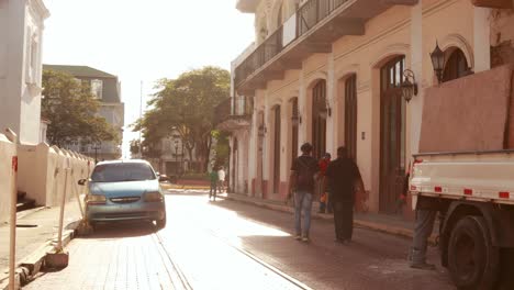 Two-men-walking-briskly-along-a-small-side-street-towards-the-Independence-Square,-the-golden-rays-of-the-morning-sun-shines-through-the-buildings,-Casco-Viejo,-Panama-City