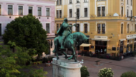 Estatua-Ecuestre-De-Hunyadi-Janos-En-Pecs,-Hungría-Con-El-Ayuntamiento-De-Pecs-En-El-Fondo-Temprano-En-La-Mañana