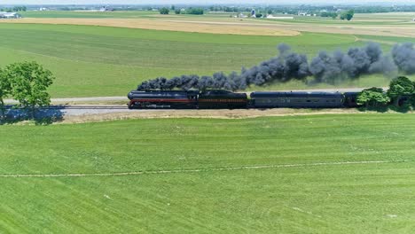 Luftaufnahme-Einer-Antiken-Dampfmaschine-Und-Personenwagen,-Die-An-Einem-Sonnigen-Sommertag-Entlang-Der-Landschaft-Fahren-Und-Rauch-Und-Drohnen-Blasen,-Die-Parallel-Dazu-Reisen