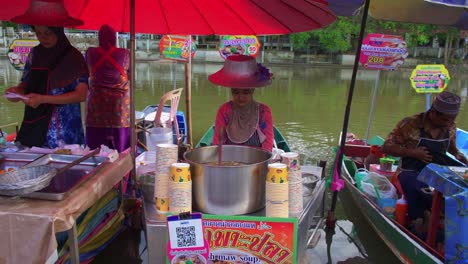 Lächelnder-Junger-Asiatischer-Arbeiter,-Der-Typisches-Thailändisches-Essen-Von-Einem-Boot-In-Einem-Schwimmenden-Markt-Verkauft