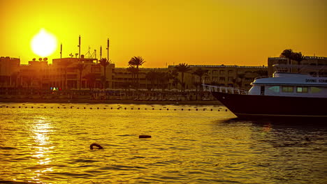 A-golden-sunset-time-lapse-over-Hurdhada,-Egypt-with-a-boat-anchored-in-the-foreground