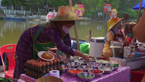 Young-Thai-woman-wearing-a-mask-and-typical-cap-preparing-her-vegetables-to-sell-at-a-local-street-stall