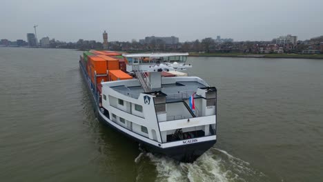 Aerial-Parallax-Shot-Around-Stern-Of-Scaldis-Container-Ship-Travelling-Along-Oude-Maas-On-Overcast-Day-In-Dordrecht