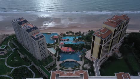 Aerial-view-of-Grand-Hotel-Ho-Tram-featuring-buildings,-swimming-pool-and-sunlight-over-ocean