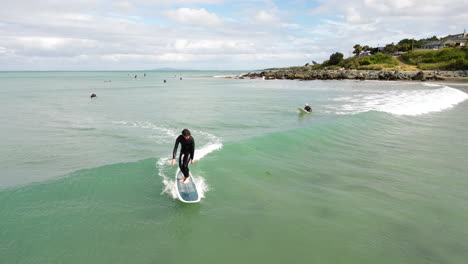 Aéreo,-Hombre-En-Traje-De-Neopreno-Surfeando-En-La-Ola-En-La-Playa-De-Riverton,-Nueva-Zelanda