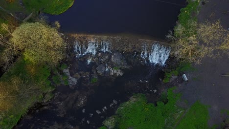 Fly-high-above-a-small-waterfall-surrounded-by-a-lush-forest-and-river