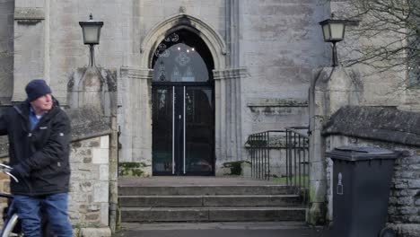 Un-Caballero-Sacando-Su-Bicicleta-De-Los-Jardines-De-La-Iglesia-En-Oakham,-Rutland,-Inglaterra