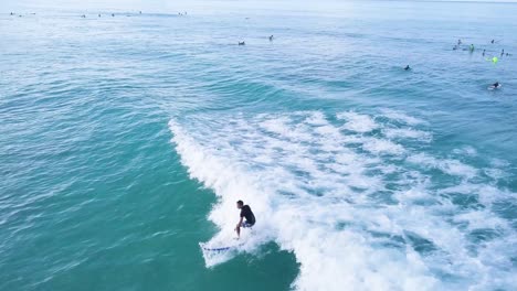 Male-surfer-carving-a-wave-at-waikiki-beach-in-honolulu-hawaii-with-crowded-waters-and-blue-skies,-AERIAL-TRUCKING-SHOT