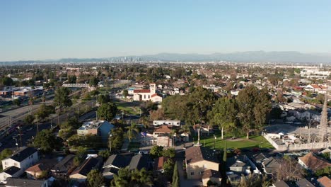 Toma-Aérea-De-Carro-Rápido-Desde-Las-Torres-De-Watts-Hasta-Las-Vías-Del-Metro-Mientras-Pasa-El-Tren-Con-El-Centro-De-Los-Ángeles-Al-Fondo