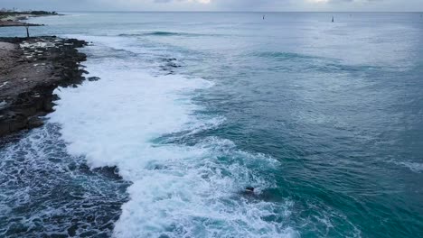 Crashing-blue-waves-and-white-sea-foam-during-sunset-in-koolina-west-oahu-honolulu-hawaii-on-a-jagged-shoreline,-AERIAL-DOLLY