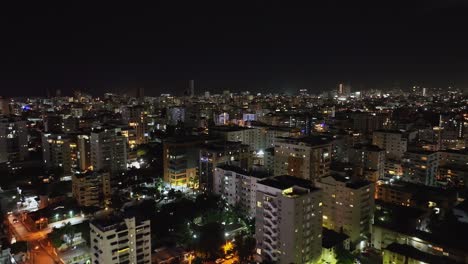 Flyover-Santo-Domingo-city-at-night-in-Dominican-Republic-with-illuminated-buildings-and-skyscrapers