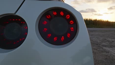 Close-up-on-rear-lamp-of-Nissan-GTR-detail-against-scenic-sunset