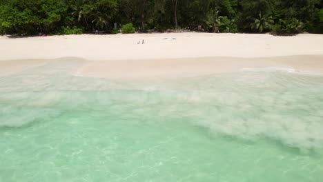 Mahe-Seychelles-Intendance-beach,-man-running-and-dive-in-ocean-wave,-sitting-clients-on-the-beach,-warm-sunny-day