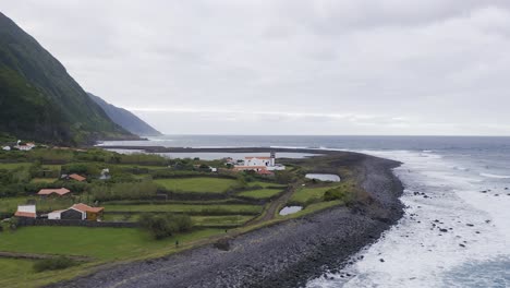Drone-orbiting-view-of-a-coastal-village,-lush-green-cliffs-landscape,-Fajã-de-Santo-Cristo,-São-Jorge-island,-the-Azores,-Portugal
