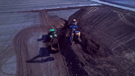 Excavator-loading-dirt-into-tractor-in-rural-landscape