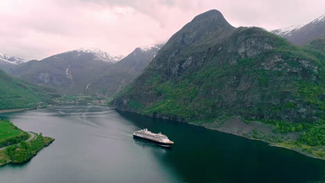 Aerial-view:-Gigantic-Cruise-Ship-on-Fjord-between-idyllic-mountains-of-Norway-with-snow-on-the-peak