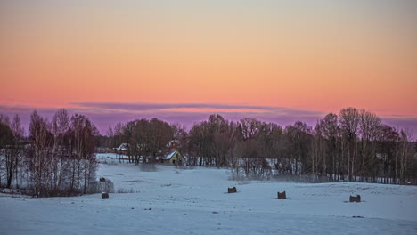 Timelapse-of-a-yellow-sky-turning-pink-over-a-snowy-landscape-with-a-cabin