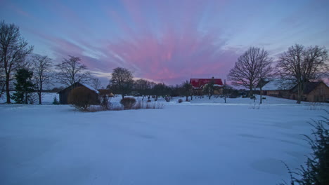 Timelapse-of-a-snowy-landscape-with-two-log-cabins-and-a-pink-sky-with-clouds-turning-blue