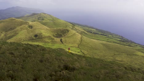 drone-orbiting-around-Asian-Malaysian-Chinese-tourist-woman-making-a-video-with-a-phone-on-a-path-on-the-edge-of-the-mountain,-on-Pico-da-Esperança,-in-São-Jorge-island,-the-Azores,-Portugal