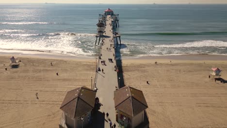 El-Video-De-Un-Dron-Captura-La-Icónica-Calle-Principal-En-Huntington-Beach,-California,-Que-Conduce-Al-Océano-Pacífico,-Mostrando-El-Famoso-Muelle-Y-El-Animado-Ambiente-De-Playa.