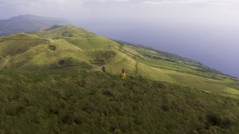 Drone-Orbitando-Alrededor-De-Una-Turista-China-Malasia-Asiática-Caminando-Por-Un-Sendero-Al-Borde-De-La-Exuberante-Montaña-Volcánica-Verde,-En-El-Pico-Da-Esperança,-En-La-Isla-De-São-Jorge,-Las-Azores,-Portugal