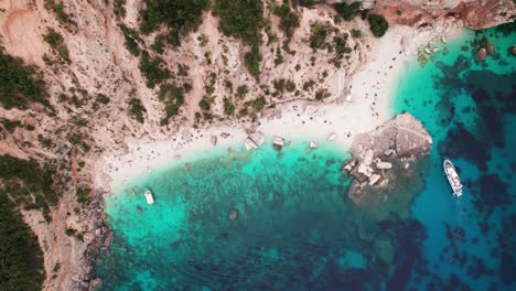 Aerial-top-down-of-tropical-beach-on-rock-coast-with-turquoise-sea,-Sardinia