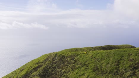 Asian-Malaysian-Chinese-tourist-woman-dancing-on-a-path-on-the-edge-of-the-mountain-with-360-camera-selfie-stick,-drone-view-on-Pico-da-Esperança,-in-São-Jorge-island,-the-Azores,-Portugal