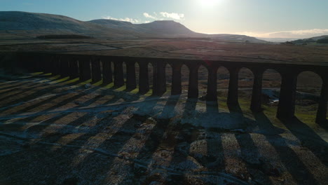 Railway-bridge-flyover-at-sunset-with-long-shadows-in-winter-at-Ribblehead-Viaduct