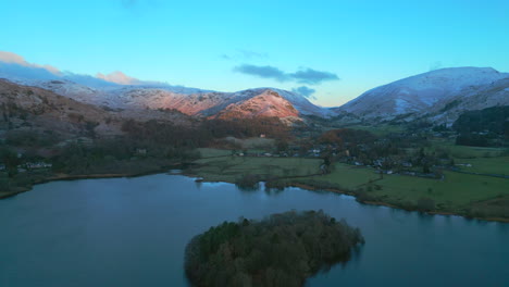 Flying-over-lake-towards-sunrise-lit-snowy-mountains-at-Grasmere-English-Lake-District