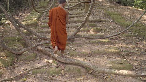 Bare-footed-Monk-in-saffron-robes-walking-over-remote-Angkorian-sandstone-rocky-pathway-through-the-jungle