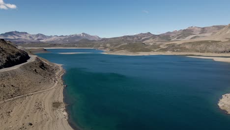 Panning-aerial-view-of-the-maule-lagoon-at-the-pehuenche-border-crossing-between-chile-and-argentina-on-a-sunny-day-with-the-andes-mountains-in-the-background