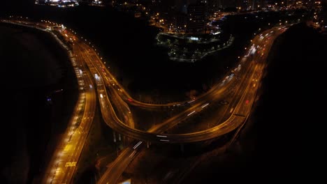 Drone-hyperlapse-of-a-coastal-overpass-that-leads-into-an-uphill-road-called-"Bajada-Armendariz"-Drone-flies-backwards-and-up-showing-the-blurring-passing-cars-head-lights