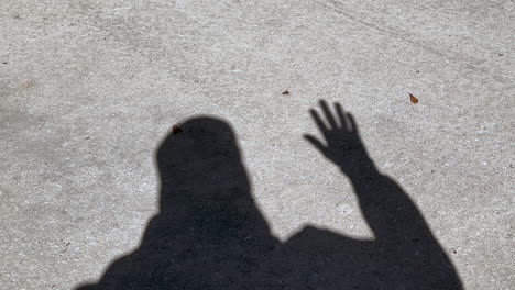 Shadow-of-man-waving-hand-that-is-open-showing-all-fingers,-standing-on-concrete