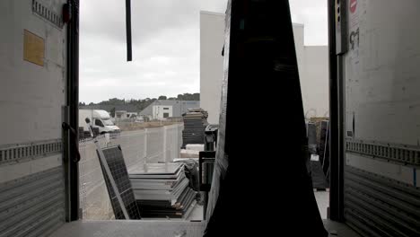 Loading-solar-panel-crates-with-a-forklift-from-inside-truck-container-box,-Dolly-out-handheld-shot