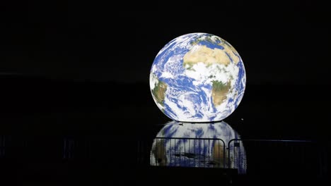 Luke-Jarram-illuminated-floating-earth-art-exhibit-reflections-in-lake-water-at-night-silhouette-barrier