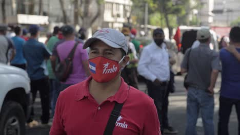 El-Hombre-Camina-En-Medio-De-Los-Manifestantes-Con-Una-Máscara-Facial-Y-Una-Camisa-Fmln---Cámara-Lenta