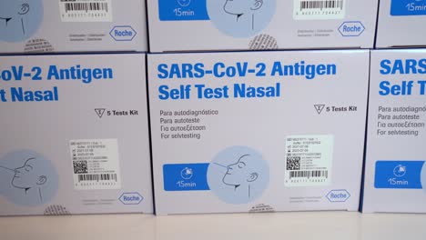 Sars-covid-antigen-self-test-nasal-by-Roche---Stacks-of-test-kits-on-white-table---Slow-moving-slider-shot-from-left-to-right---Closeup-macro