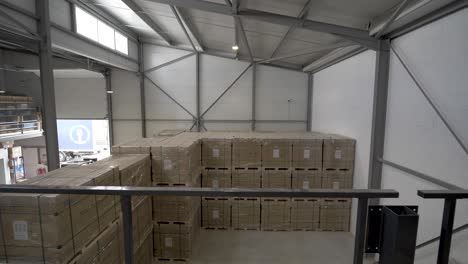 Boxed-crates-full-of-photovoltaic-roof-solar-panels-in-large-warehouse,-Tilt-down-dolly-in-shot